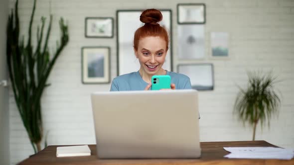 Happy Redhead Young Woman Is Enjoying Success While Looking Mobile Phone.