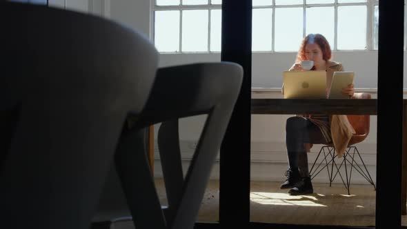 Front view of young caucasian businesswoman working on digital tablet and laptop in a modern office