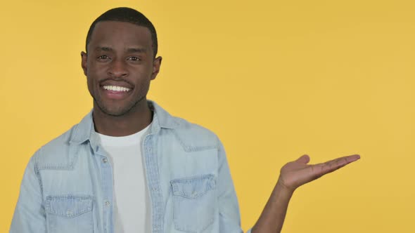 Young African Man Holding Product on Palm Yellow Background
