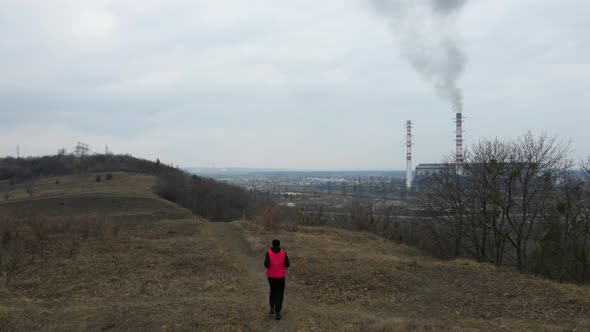 Aerial view from drone of man, running near Plant pipes pollute atmosphere,