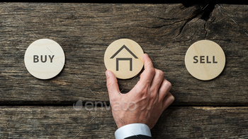 businessman placing wooden cut circle with house shape on it in between Buy and Sell signs.