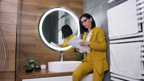 Brunette in Stylish Clothes Sitting Near the Bathroom Mirror and Watching at the Business Papers