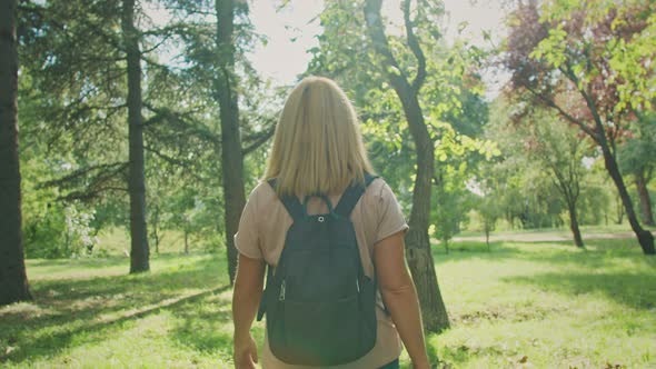 A girl walks in a large green forest