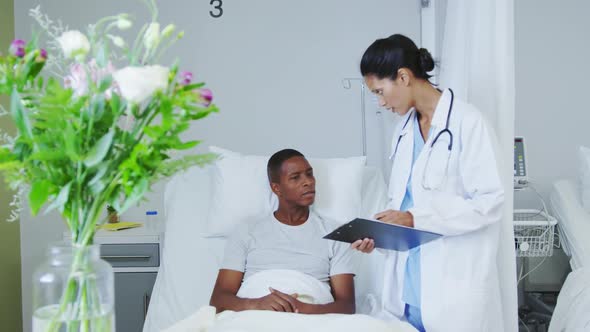 Front view of African american female doctor talking with male patient in ward at hospital