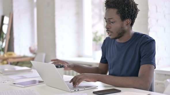 Young African Man Drinking Coffee and Working on Laptop