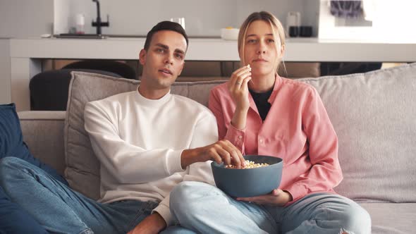 Happy Young Couple Watching Funny Show on TVeating Popcorn at Home Lying on Sofa Together. People