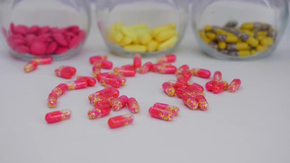 Slowly dropping capsules over a white table with colorful tablets in transparent glass bottle around