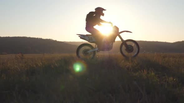 Two Motorcyclists Passing Through Large Field with Beautiful Sunset at Background