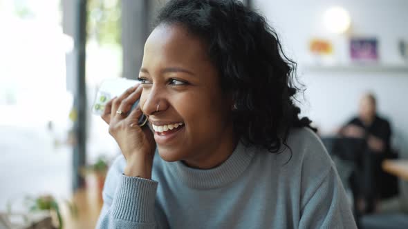 Laughing African woman wearing blue sweater listening voice message on phone