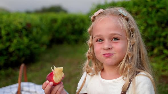 Funny and Cheerful Girl Eating Fruit on the Picnic