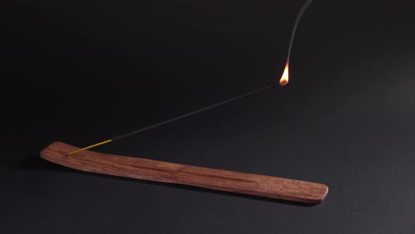 A Woman's Hand Sets Fire To an Aromatic Stick in a Stand on a Black Background. Spiritual Smoke