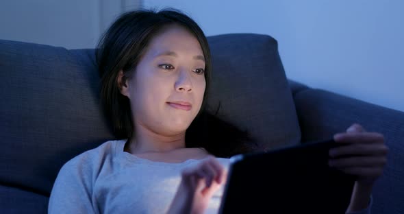 Woman use of tablet computer and lying on sofa at night