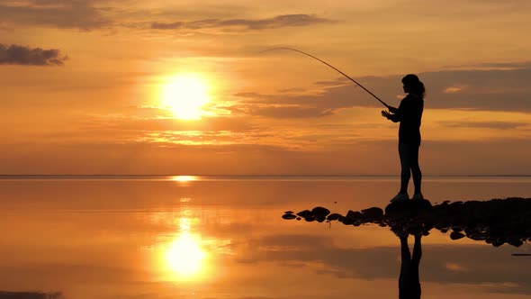 Woman Fishing on Fishing Rod Spinning at Sunset Background