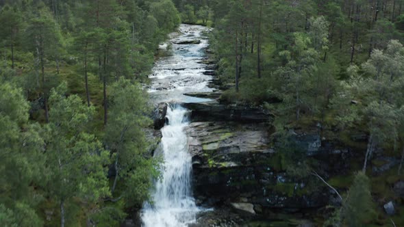 Aerial of sparkling waterfall in protected area tilting up to reveal mountains and valley