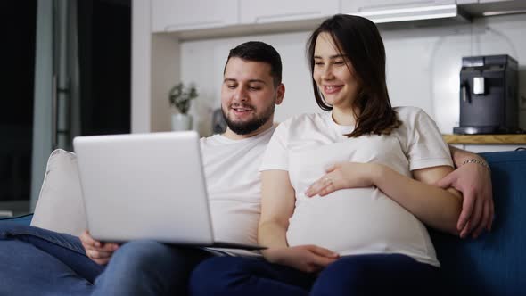 Lovely Pregnant Woman and Man Watching Comedy Film on Laptop