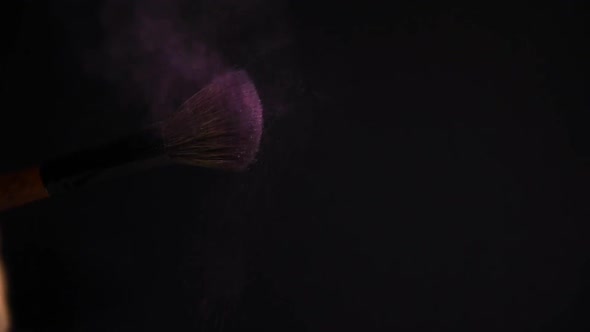 slow motion of a make up brush with pink powder explosion and burst on black background