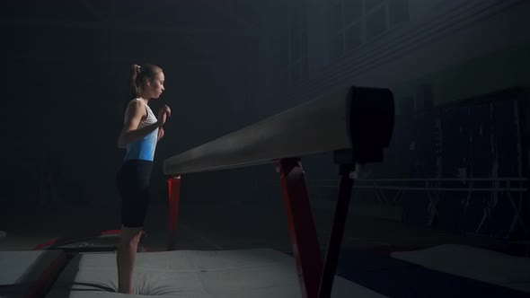 Training of Artistic Gymnastics Adolescent Sporty Girl is Sitting on Balance Beam in Dark Sports