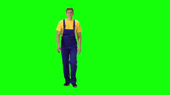 Young Man in Uniform, Yellow T-shirt and Blue Jumpsuit Going Against Green Background.