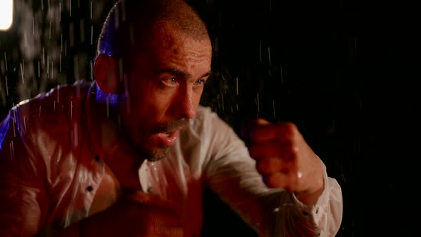 a Man in an Unbuttoned White Shirt is Boxing in Streams of Water on a Dark Background