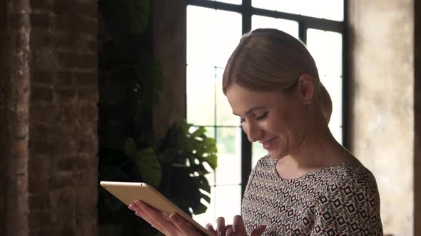 Young attractive smiling caucasian woman uses tablet with window background. 