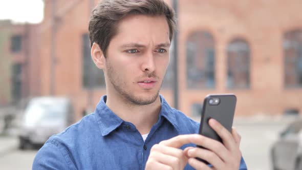 Outdoor Portrait of Young Man Upset By Loss While Using Smartphone
