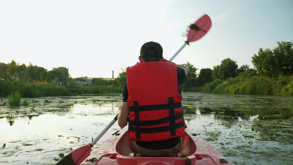 Sportive strong man in life vest is rowing in kayak on river. Water tourism. Sport rowing