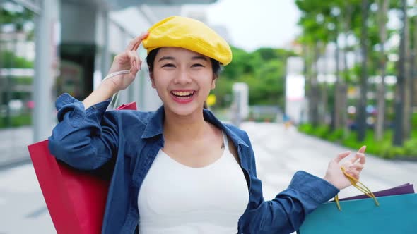 Smiling young Asian woman with shopping colour bags over mall background.