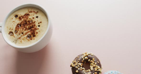 Video of donuts with icing and cup of coffee on pink background