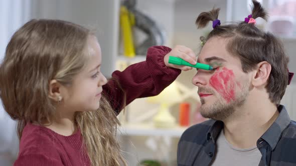 Side View Closeup of Cheerful Pretty Girl Painting Father Eyelids with Green Marker Smiling