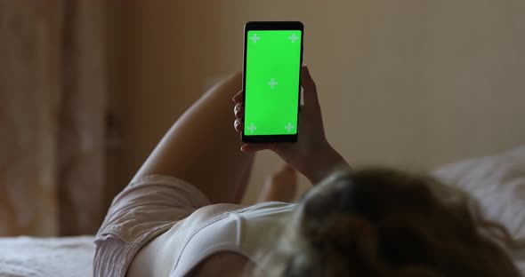 Mockup of Woman Using Smartphone Green Screen Lying on a Bed