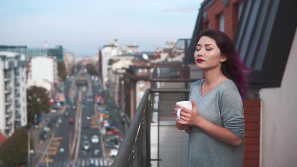 Pretty Young Woman in Stays on Balcony Holds Cup of Hot Coffee or Tea