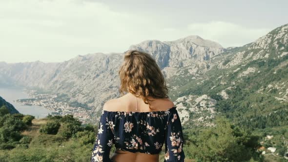 Young curly-haired woman standing on the background of the mountains