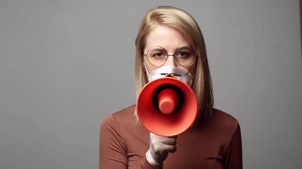 Blonde woman in protective mask with megaphone on grey background