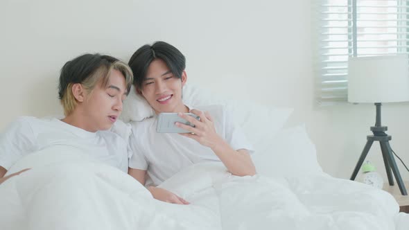 Asian attractive male gay couple use mobile phone watch movie on bed.