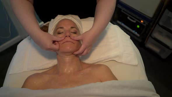 Massage therapist rubs cream onto her client’s face as part of her facial massage. Steadicam shot.