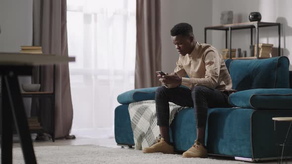 Young Black Man is Playing Video Game in Smartphone Sitting at Home Alone Afroamerican Guy