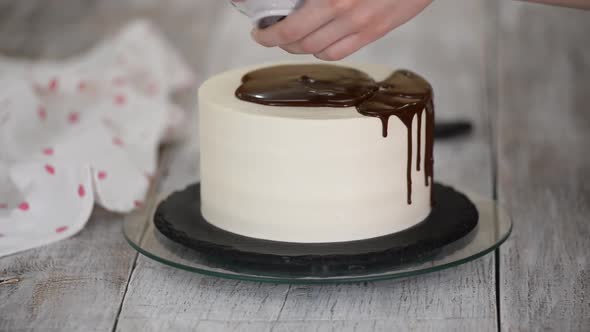 Closeup of a Pastry Chef Pouring Liquid Chocolate on a White Cream Cake