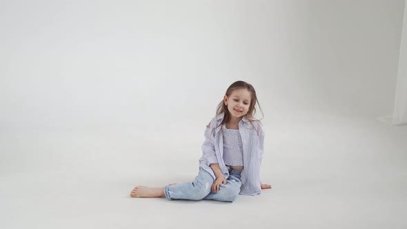 Little Girl with Long Hair in Jeans and Shirt Posing Against a White Background