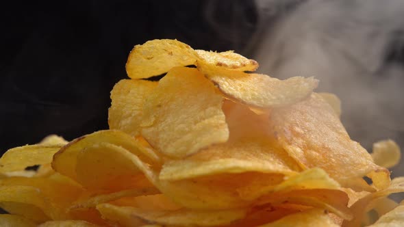 Craft crispy hot potato chips with smoke rotating on black background close up. Golden fried