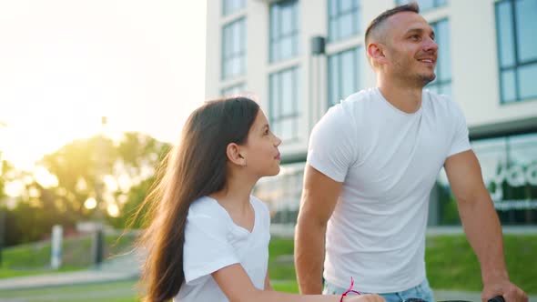 Dad is Teaching Daughter How to Ride Bicycle at Sunset