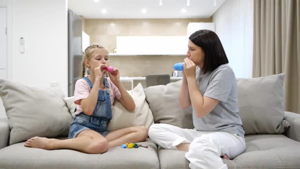 Mother and Teenage Daughter Having Fun Blowing Balloons Sitting on Couch in Living Room Slow Motion