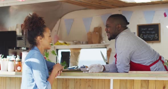 Happy african american male food truck owner talking over counter to smiling female customer