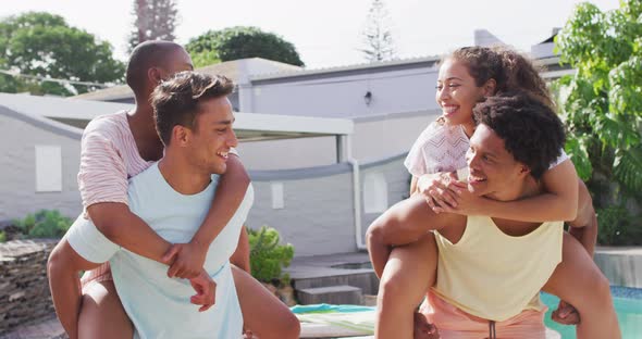 Two happy diverse male friends carrying piggyback female friends in backyard at pool party