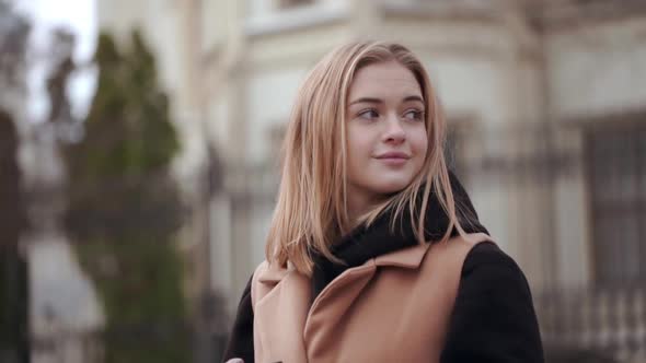 Street Shot of Cute Curious Caucasian Woman Wearing Beige Coat Looking Around While Walking Trough