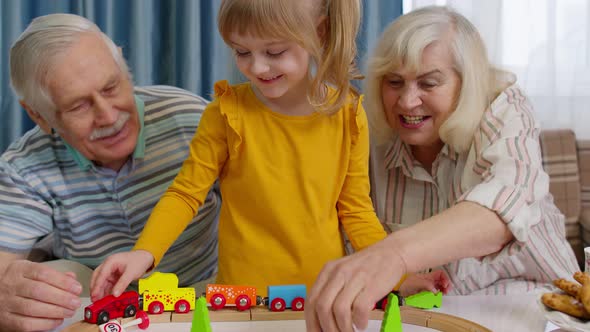 Senior Grandparents with Child Kid Granddaughter Playing Game Riding Toy Train on Railway at Home