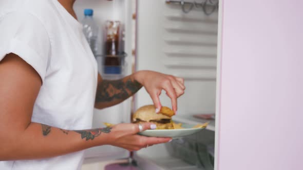 Unknown Female Holding Plate with Hamburger and French Fries Opening Fridge Taking Chicken Nuggets