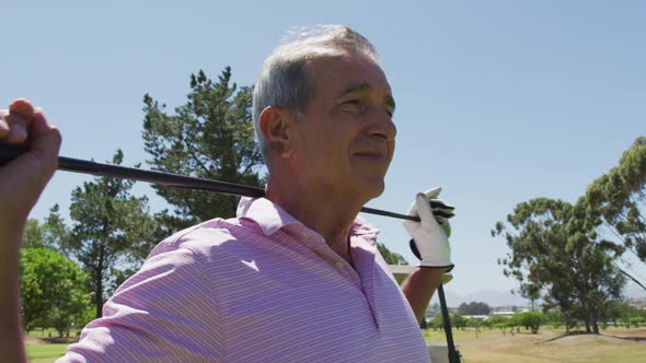 Portrait of caucasian senior man with golf club smiling at golf course on a bright sunny day