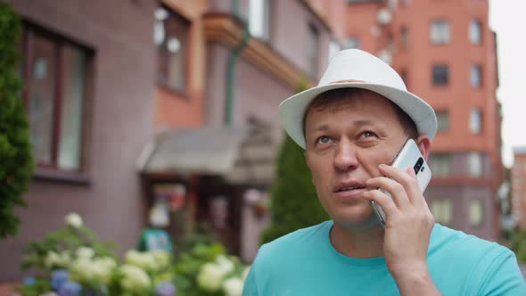 Portrait of a young man in a hat talking on a mobile phone in the street, camera tracking