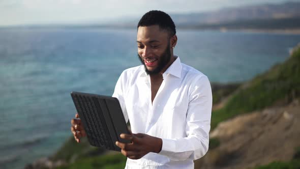 Happy Smiling African American Gay Man Using Video Chat on Tablet Standing on Picturesque Blue Azure