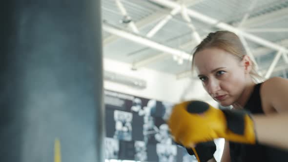 Young Woman in Boxing Gloves Training with Punching Bag in Modern Gym